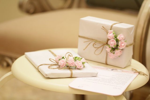 Regalos especiales para invitados envueltos en papel blanco roto y atados con cenefa dorada y rosas rosas